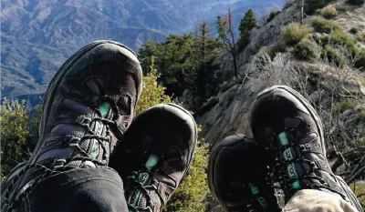 Two people wearing hiking boots sitting on top of a mountain